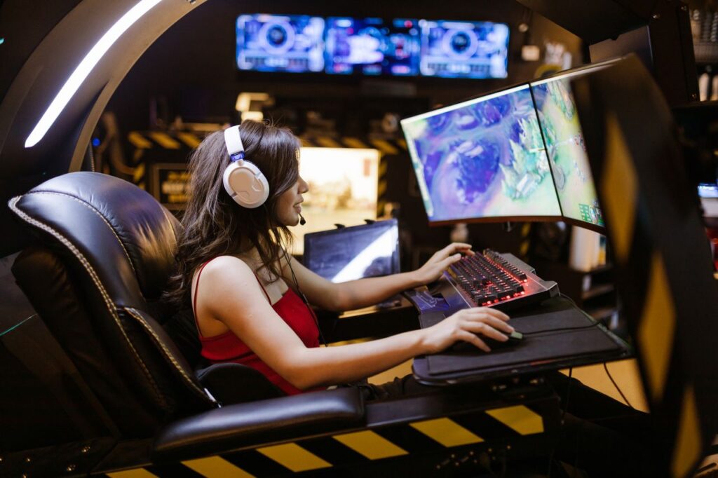 Gamer wearing a headset playing a multiplayer PC game on dual monitors at a gaming station.